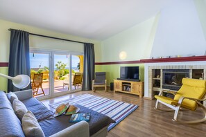 A living room with a sofa, a television, a fireplace, and a view through the glass doors. - Quinta da Belavista 55 by CoolHouses (Luz)