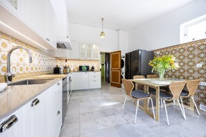 Een moderne keuken met witte kasten, een marmeren aanrechtblad en een eethoek met rieten stoelen.