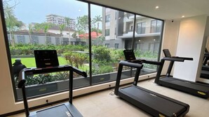 A gym with treadmills and a laptop on a desk, large windows with a view of buildings and greenery. - Peravi at The Signature (Accra)