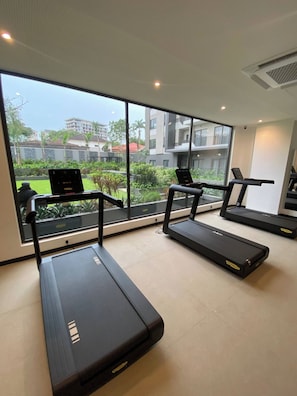 A gym with treadmills and a laptop on a desk, large windows with a view of buildings and greenery. - Peravi at The Signature (Accra)
