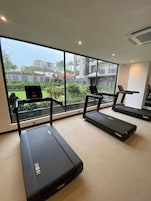 A gym with treadmills and a laptop on a desk, large windows with a view of buildings and greenery.