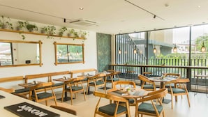 Ein Restaurantinnenraum mit Holztischen, gepolsterten grünen Sitzplätzen und großen Fenstern mit Blick ins Freie.