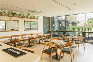 En restaurang med en inredning som präglas av trämöbler, gröna, vadderade sittplatser och stora fönster som ger utsikt över omgivningen.