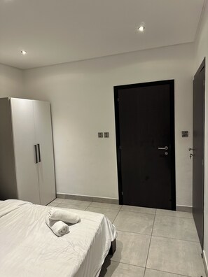 A bedroom with a bed, a wardrobe, a door, and a light switch on the wall. - Peravi at The Signature (Accra)