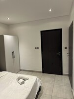 A bedroom with a bed, a wardrobe, a door, and a light switch on the wall.
