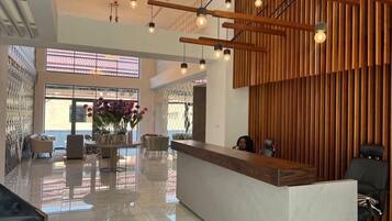 A modern reception area with a wooden reception desk, a seating area with chairs, and a large window providing natural light.
