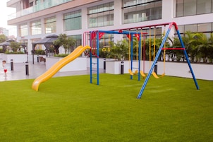 An outdoor playground with a slide and swings, surrounded by a well-maintained lawn and a building in the background.