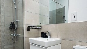 A modern bathroom with a glass shower enclosure, a white sink, and a toilet. - Peravi at The Signature (Accra)