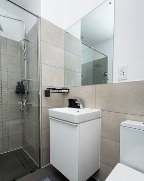 A modern bathroom with a glass shower enclosure, a white sink, and a toilet. - Peravi at The Signature (Accra)