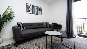 A modern living room with a grey sofa, a round black coffee table, a potted plant, and a framed abstract art piece on the wall. - Peravi at The Signature (Accra)