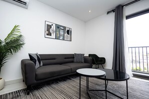 A modern living room with a grey sofa, a round black coffee table, a potted plant, and a framed abstract art piece on the wall. - Peravi at The Signature (Accra)