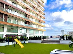 A multi-story residential building with a playground, a swimming pool, and a well-maintained lawn. - Peravi at The Signature (Accra)