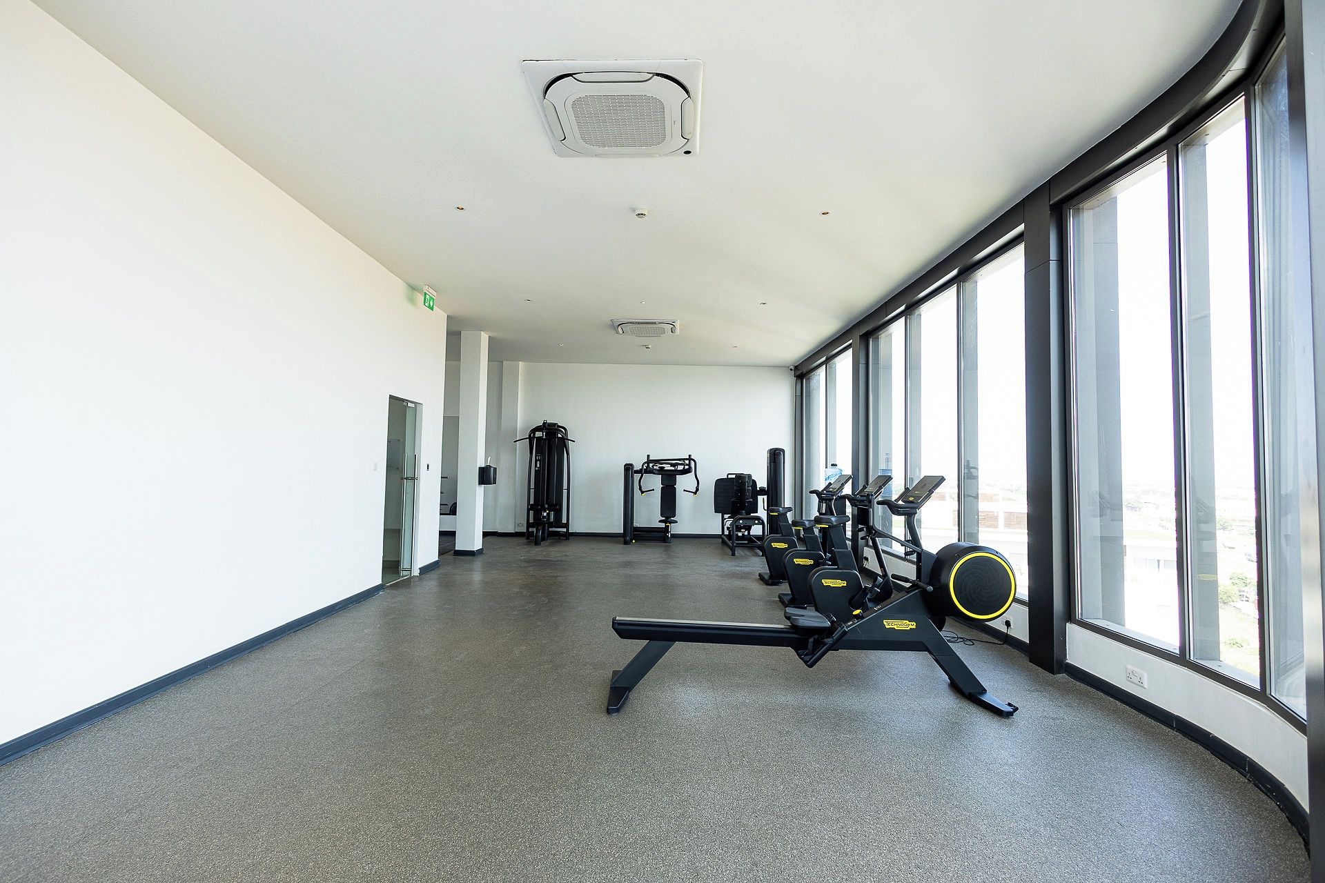 A gym with cardio machines, weightlifting equipment, and large windows.