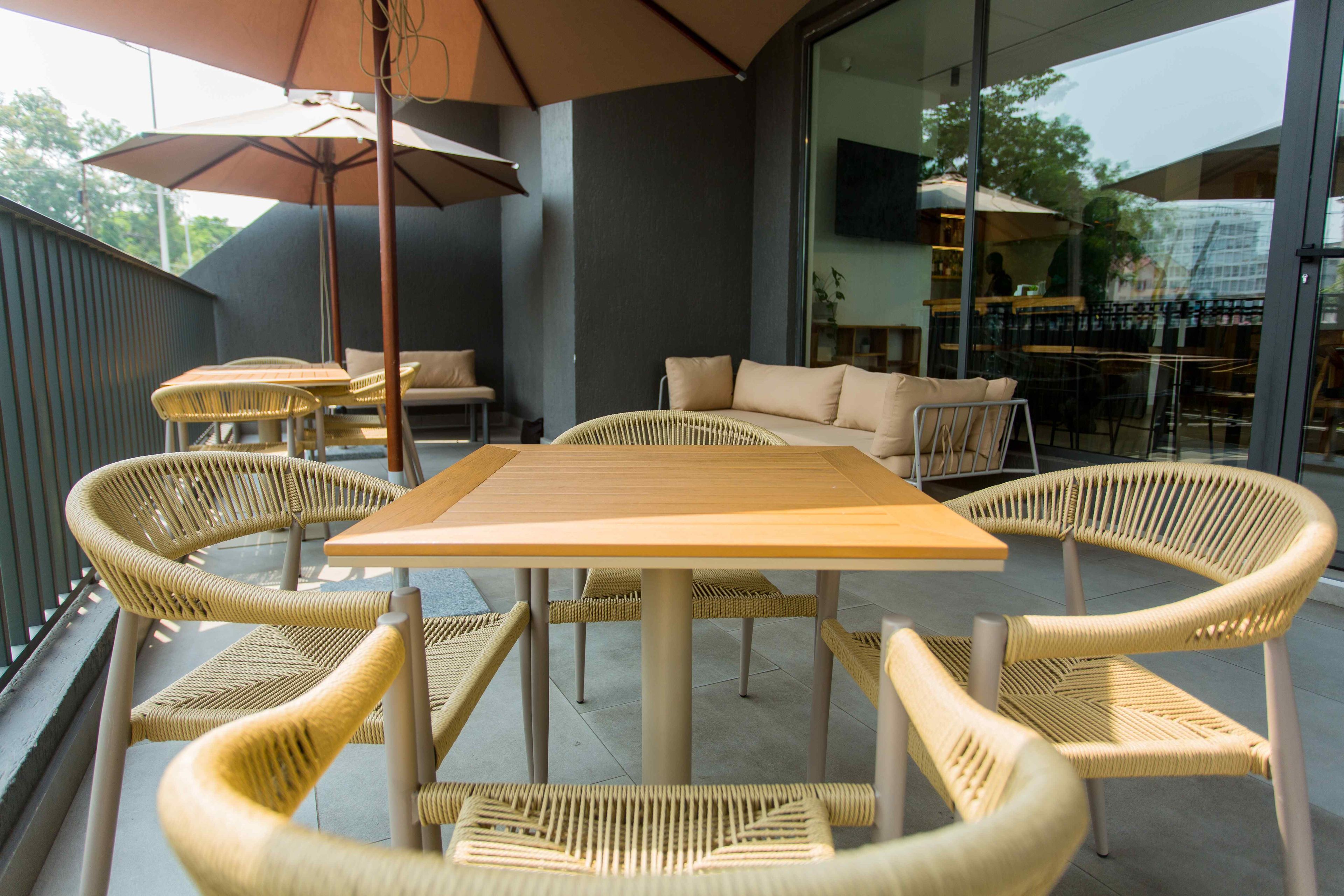 Un área de estar al aire libre con una mesa de madera y sillas de mimbre, un sofá y una sombrilla.