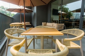 Un área de estar al aire libre con una mesa de madera y sillas de mimbre, un sofá y una sombrilla.
