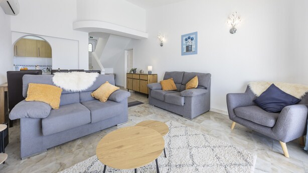 Una sala de estar moderna con sofás grises, una mesa de centro de madera y una alfombra blanca.