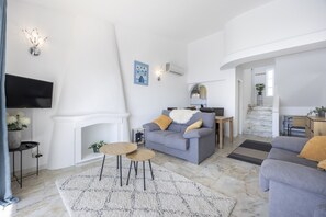 A modern living room with a grey sofa, a flat-screen TV, a fireplace, and a staircase leading to an upper level.