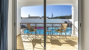 Un balcón con piscina, dos sillas de mimbre y una mesa con una botella y vasos.