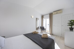 A hotel room with a bed, a chair, a wardrobe, and a potted plant.