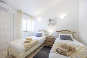 A room with two beds, a window, a door, and a wall-mounted light fixture. - Casa Lília | Mte S Pedro 2 (Luz)