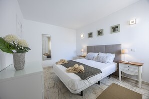 Un dormitorio moderno con cama, mesitas de noche, un espejo y obras de arte en la pared.