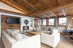Ein gemütliches Wohnzimmer mit Kamin, Holzbalkendecke und einem an der Wand befestigten Fernseher.