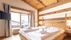 A wooden-framed room with a bed, a flat-screen TV, and a window with curtains. - Penthouse with 3 bedrooms (Reith bei Kitzbühel)