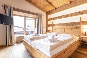 Ein Zimmer mit Holzbalken, einem Bett, einem Flachbildfernseher und einem Fenster mit Vorhängen.