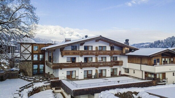 A multi-story hotel with balconies, a covered outdoor area, and a view of snow-covered mountains. - Penthouse with 3 bedrooms (Reith bei Kitzbühel)