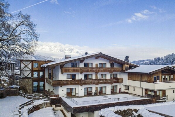 Ein mehrstöckiges Hotel mit Balkonen, einem überdachten Außenbereich und Blick auf schneebedeckte Berge.