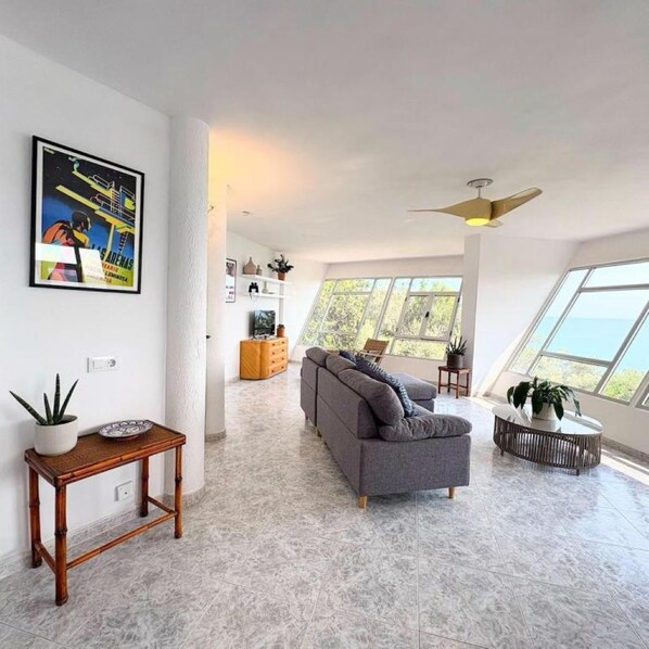 Un salon moderne avec un canapé gris, une table en bois et un ventilateur de plafond.