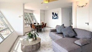 Een moderne woonkamer met een grijze bank, een ronde salontafel en een eethoek met een glazen tafel en stoelen.