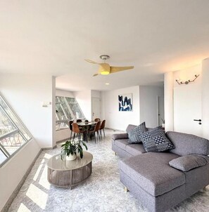 Un salon moderne avec un canapé gris, une table basse ronde et un coin repas comprenant une table et des chaises en verre.