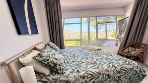Een slaapkamer met een groot bed, een nachtkastje, een stoel en uitzicht op een heuvel.