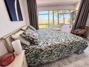 Une chambre avec un grand lit, une table de chevet, une chaise et une vue sur une colline.
