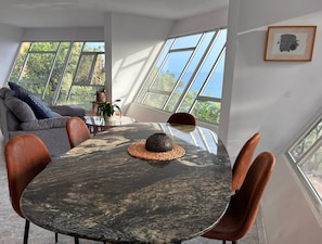 A dining area with a round table, chairs, and a view through large windows.