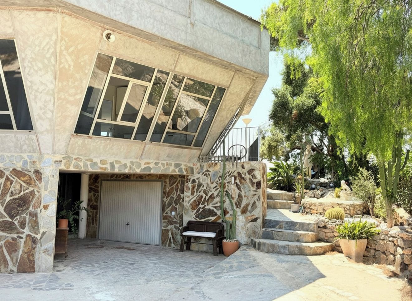Un edificio moderno con fachada de piedra, ventanas amplias y un patio con mobiliario exterior.