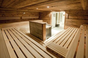A wooden sauna room with benches and a central stone structure. - Penthouse with 2 bedrooms (Reith bei Kitzbühel)