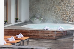 Un bain à remous avec des serviettes, une terrasse en bois et un mur en pierre.