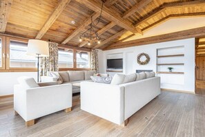 A modern living room with a wooden ceiling, white sofas, a flat-screen TV, and a fireplace. - Penthouse with 2 bedrooms (Reith bei Kitzbühel)