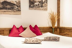 A bed with red and patterned pillows, a wooden headboard, and two black-and-white photographs on the wall. - Penthouse with 2 bedrooms (Reith bei Kitzbühel)