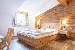 A wooden-framed bedroom with a bed, bedside tables, and a window with curtains. - Penthouse with 2 bedrooms (Reith bei Kitzbühel)