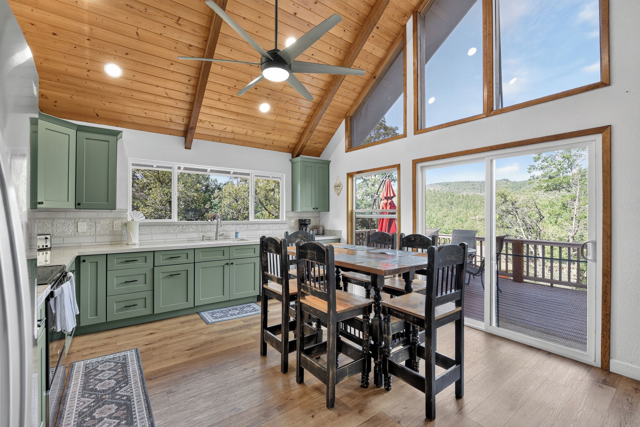 A spacious kitchen with a dining area, large windows, and a ceiling fan.