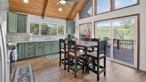 A spacious kitchen with a dining area, large windows, and a ceiling fan. - Pine Cabin w View, Fireplace, Deck & Game Room (Pine)