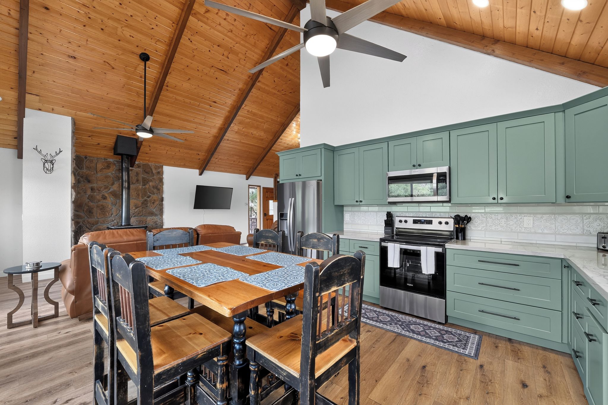A spacious kitchen with a stone wall, a dining area with a wooden table, and a ceiling fan.
