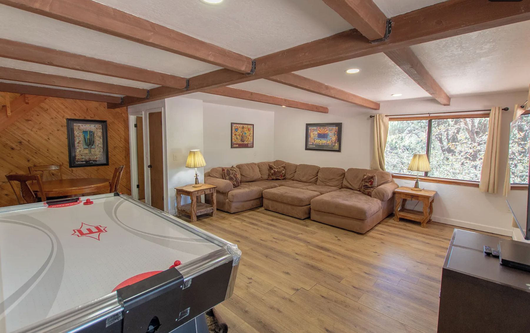 A cozy living room with a pool table, wooden beams, a sectional sofa, and framed artwork on the walls.