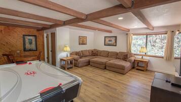 A cozy living room with a pool table, wooden beams, a sectional sofa, and framed artwork on the walls.