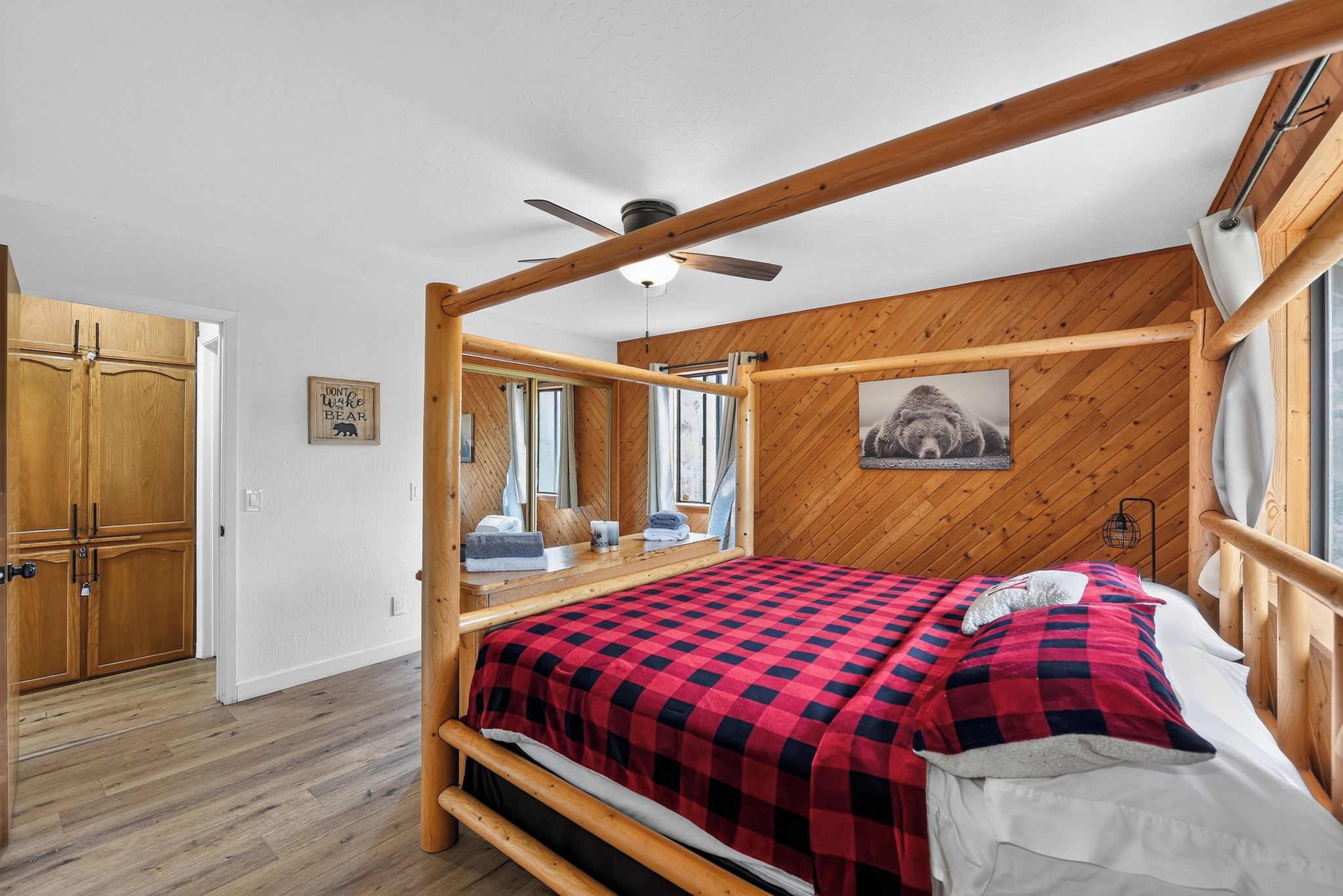 A bedroom with a four-poster bed, wooden walls, a ceiling fan, and a large window.
