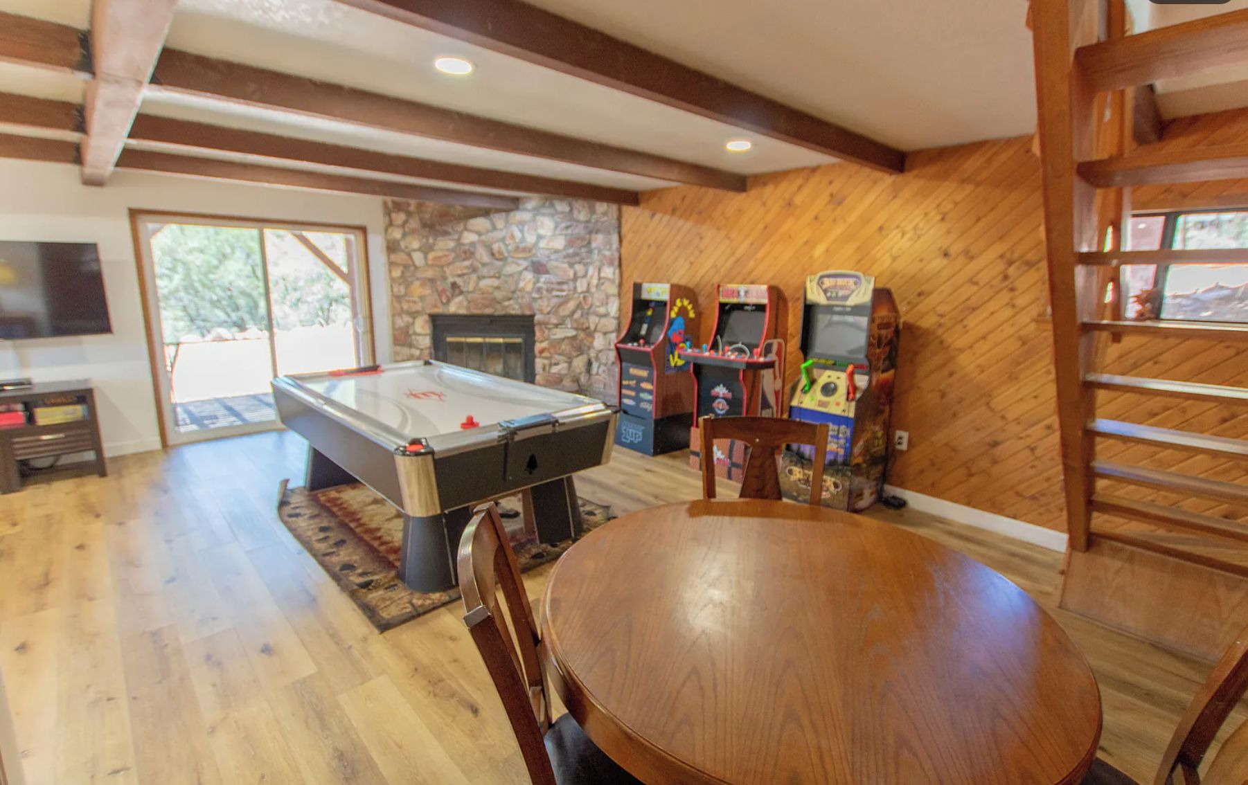 A room with a pool table, arcade machines, a fireplace, and a dining area.