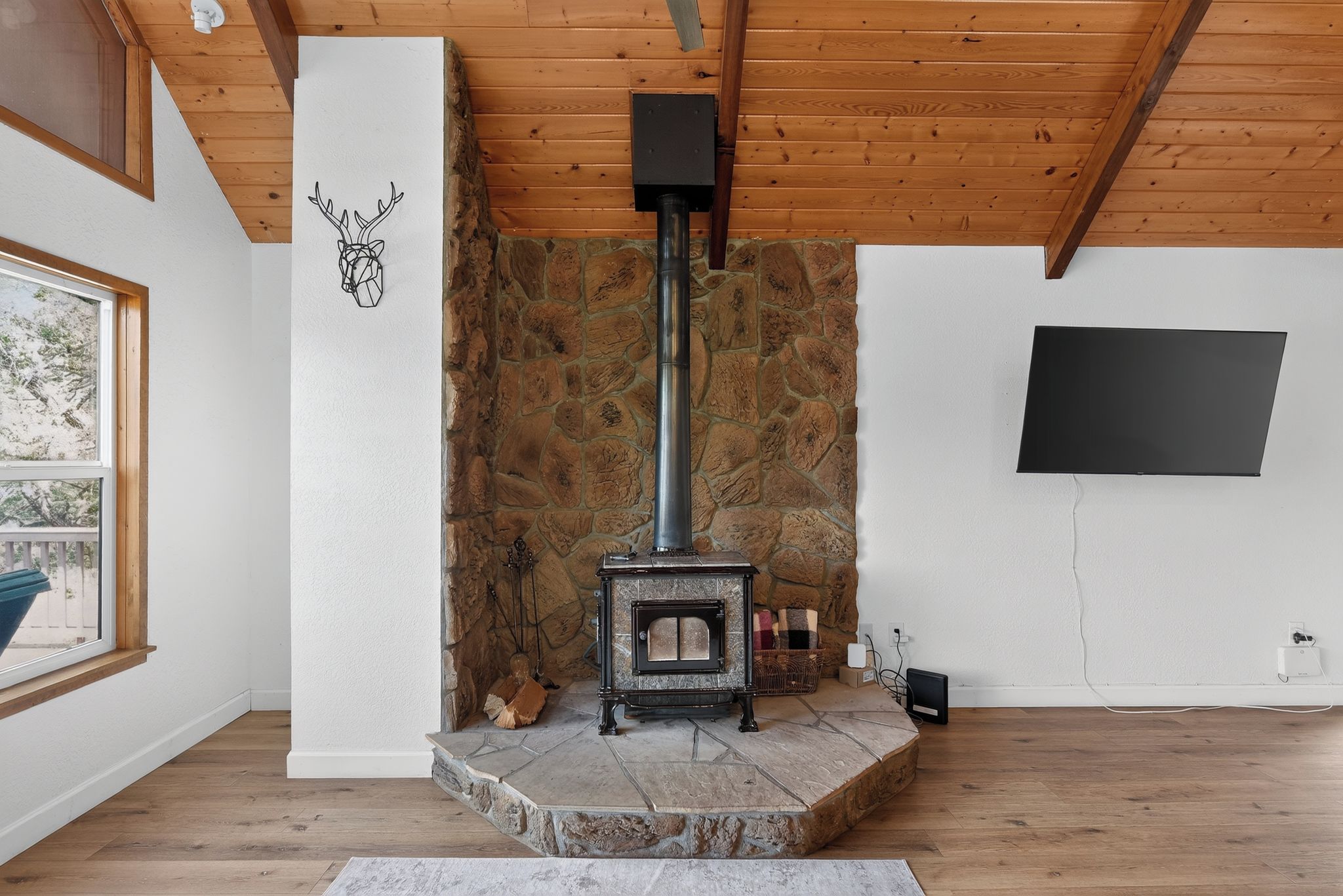 A room with a stone wall, a fireplace, a window, and a flat-screen TV mounted on the wall.